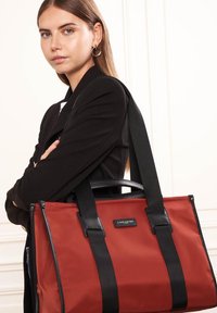 Borsa tote in tessuto rosso con dettagli in pelle nera, doppi manici superiori e cinturini regolabili. Dotata di un'etichetta con marchio e design strutturato.