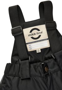 Schwarzer wasserdichter Overall mit verstellbaren Trägern, versehen mit einem beigen Etikett, das Pflegehinweise und Markenlogo zeigt. Weiche Textur, robustes Material.