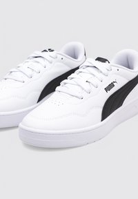 Zapatillas blancas hechas de material sintético, con una franja lateral negra y logo, puntera redonda, cordones planos y suela de goma texturizada.