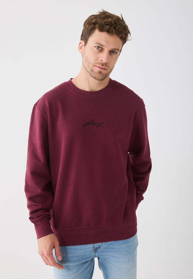 Sweatshirt bordeaux avec un col rond, arborant un logo noir brodé sur la poitrine. Fabriqué en tissu doux avec des poignets et un ourlet côtelés.