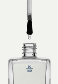 Bouteille de vernis à ongles en verre transparent avec une forme plate et rectangulaire, col argenté et étiquette blanche indiquant "80/100". Pinceau trempé, goutte se formant.