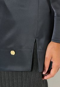 Top in tessuto di raso nero con una spaccatura laterale, caratterizzato da un accento del logo dorato rotondo vicino all'orlo, abbinato a un pantalone con motivo a spina di pesce.