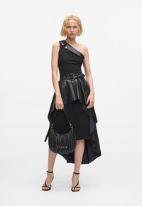 Svart ensidig kjole med peplum-skjørt, skinnfølelse og asymmetrisk kant. Kombinert med en svart flettet håndveske og sandaler med stropper.