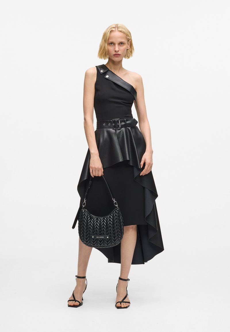 Svart ensidig kjole med peplum-skjørt, skinnfølelse og asymmetrisk kant. Kombinert med en svart flettet håndveske og sandaler med stropper.