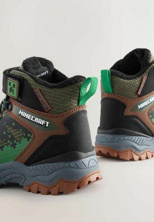Stivaletti a tema Minecraft in verde, nero e marrone. Presentano materiali testurizzati, un colletto imbottito e un logo prominente sul lato.