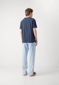 Navyblauwe katoenen T-shirt met een ronde hals, gecombineerd met losse lichtblauwe jeans en bruine instapschoenen. Eenvoudig ontwerp, geen zichtbare patronen.