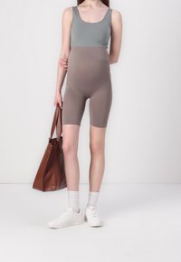 Maternity bodysuit in green on top and brown below, paired with brown tote bag. White sneakers and crew socks complete the look.