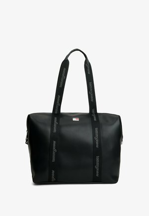 Czarna torba typu tote z długimi czarnymi uchwytami z nadrukiem "tommyjeans" oraz mała naszywka z logo Tommy Jeans z przodu na środku.