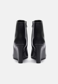 Bottines en cuir noir avec un talon bloc haut, présentant une texture lisse et une fermeture à glissière sur le côté. La vue arrière met en avant un design épuré.