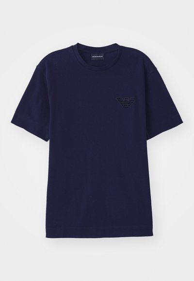 Marineblaue Baumwoll-T-Shirt mit kurzen Ärmeln, das ein strukturiertes, gesticktes Logo in Form eines Adlers auf der linken Brust zeigt.