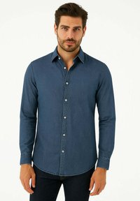 Camicia in denim blu scuro con maniche lunghe, colletto button-down e patta con bottoni frontale. Presenta un orlo curvo e dettagli di cucitura visibili.