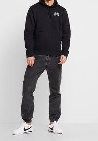 Svart huvtröja med framficka, med en grafisk design. Kombineras med grå smala jeans och vita sneakers.