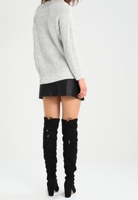 Maglione grigio lavorato a maglia, gonna mini in pelle nera e stivali alti in suede neri con lacci. Texture morbide e colori a contrasto.