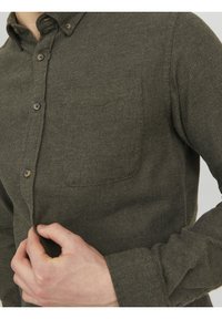 Camicia verde oliva con bottoni realizzata in tessuto testurizzato, dotata di una singola tasca sul petto e dettagli di cucitura visibili sulla patta e sui polsini.