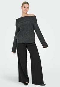 Sweter w kolorze ciemnoszarym z dzianiny z dekoltem off-shoulder, z prążkowaną teksturą i szerokimi rękawami, zestawiony z luźnymi czarnymi spodniami i płaskimi czarnymi butami.