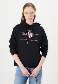Black cotton hoodie with a front pocket, drawstring hood, and a logo featuring red and blue accents. Soft texture, casual fit.