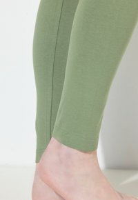 Zielone legginsy wykonane z miękkiego, elastycznego materiału, o dopasowanym kroju z gładkim wykończeniem i subtelnym detalem szwów przy kostce.