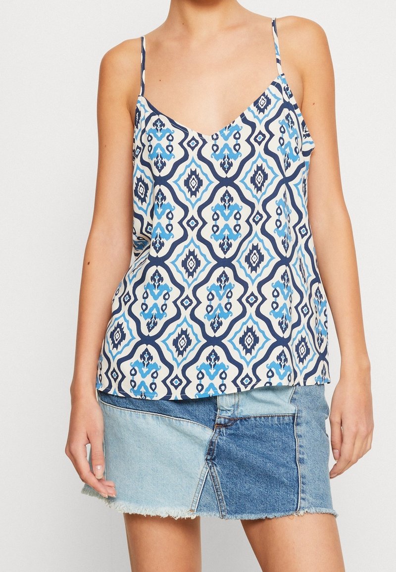 Žena v bezramínkovém vzorovaném topu s modro-bílými geometrickými tvary a dvoubarevných patchworkových džínsových minisukních.