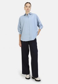 Camicia azzurra chiaro con bottoni, maniche lunghe, tessuto morbido, vestibilità rilassata, abbinata a pantaloni a gamba larga blu navy scuri e scarpe color crema.