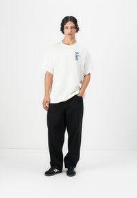 White cotton t-shirt with blue graphic design on chest, paired with loose black denim pants, and black sneakers with white stripes.