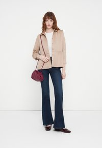 Light beige button-up jacket with a peplum design, paired with dark flared jeans. A maroon mini bag adds a contrasting accent.