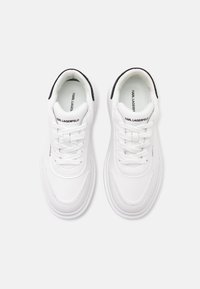 Paire de baskets blanches Karl Lagerfeld avec languettes de talon noires et languettes brandées, vue de dessus sur un fond uni.