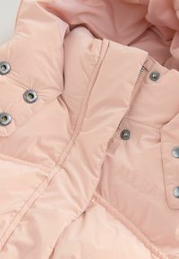 Giacca imbottita rosa con una texture lucida, dotata di bottoni a pressione argentati e cuciture rinforzate. Nome del marchio "ALLSAINTS" in rilievo.