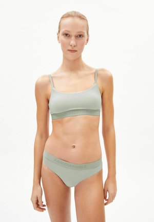 Jeune femme aux cheveux blonds portant un soutien-gorge de sport vert menthe et des sous-vêtements assortis avec la marque « ARMEDANGELS » sur les ceintures.