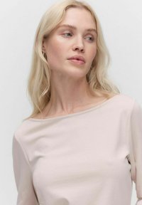Helles rosa Off-Shoulder-Top aus weichem Stoff, mit lockerer Passform und glatter Textur. Einfaches Design ohne sichtbare Muster.