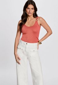Coral tank top with metallic sheen, featuring decorative shoulder straps and combined with high-waisted white wide-leg trousers with pockets.