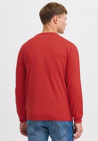 Czerwony sweter, ściągacz na dole i przy mankietach, okrągły dekold, gładka tekstura, noszony z niebieskimi dżinsami, widok z tyłu, prosty design bez wzorów.
