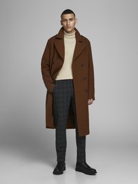 Manteau en laine brun avec un design croisé, associé à un col roulé crème et un pantalon à carreaux gris foncé. Bottes noires à lacets.