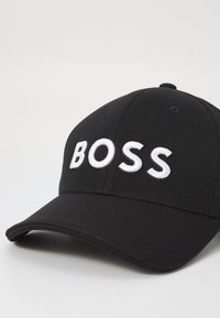 Fekete baseball sapka, strukturált dizájnnal, fehér hímzett "BOSS" felirattal az elején. Simaságú szövet textúra.