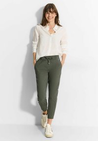 Witte, V-hals, lange mouwen, knoopsluiting shirt met verticale strepen; groene, trekkoord, tapering broek; witte sneakers.