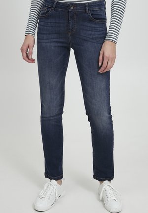 Tmavě modré slim-fit džíny z džínoviny s mírně vybledlou texturou, vybavené pěti kapsami a zapínáním na knoflík, doplněné o bílé tenisky.