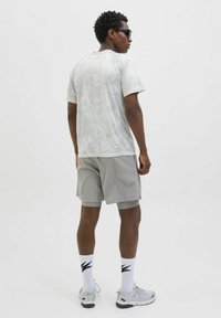 Vaaleanharmaa lyhythihainen paita, jossa on hienovarainen kuvio, yhdistettynä sopiviin sorteihin. Päällä harmaat urheilukengät ja valkoiset sukat, joissa on mustia yksityiskohtia.