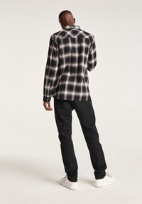 Camicia di flanella a quadri bianco e nero con maniche lunghe e polsini con bottoni, indossata con pantaloni scuri e sneakers bianche. Tessuto morbido.