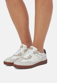 Weiße und beige Sneakers mit strukturierten Mustern, weißen Schnürsenkeln und braunen Gummisohlen. Der Markenname "MARIAMARE" ist an der Seite sichtbar.