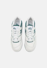 Valged sneakerid smaragdrohe aktsentidega, millel on sile nahast ülemine osa, aukude detailid varvaste piirkonnas ja ikooniline bränding külgedel.