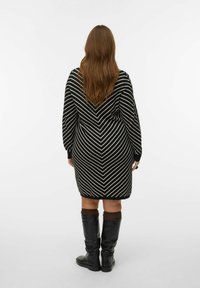 Robe pull à rayures noires et blanches avec un motif en V, manches longues et poignets côtelés, associée à des bottes noires montantes.