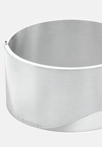 Bracciale in acciaio inossidabile con finitura spazzolata, caratterizzato da un design curvo e morbido e un discreto logo Calvin Klein inciso sul bordo.