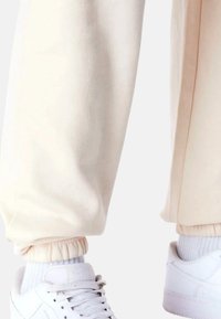 Cremefarvede joggers lavet af blødt stof har elastiske manchetter ved anklerne. Parret med hvide sneakers.
