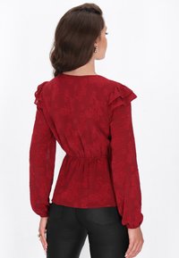 Rote Bluse mit floralem Muster, Rüschendetails an den Schultern, langen Ärmeln und elastischem Bund. Glattes Material mit einer figurbetonten Silhouette.