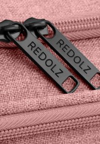 Tejido texturizado rosa con dos tiradores de cremallera negros etiquetados como "REDOLZ". Las cremalleras son suaves y tienen un borde de tela a juego.