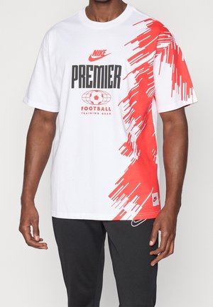 Mann trägt weißes Nike Premier Fußball-Trainings-T-Shirt mit rotem, abstraktem Pinselstrich-Design auf der rechten Seite und schwarzer Hose.