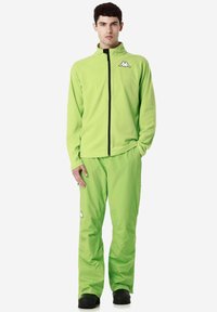 Giacca e pantaloni in pile di un vivace verde, con colletto alto e chiusura a zip. Dettagli del logo bianco su entrambi i pezzi. Texture liscia.
