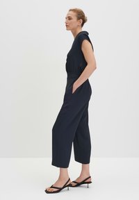 Marineblauwe jumpsuit met korte mouwen, taps toelopende pijpen en zijzakken. Zachte stof met een gladde textuur en een ingezette taille-afwerking.