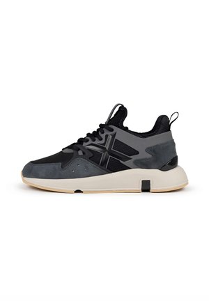 Zapatilla negra y gris que presenta una combinación de materiales de malla y ante, una suela gruesa y acentos geométricos en los laterales.