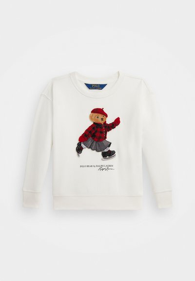 Kremfarget hettegenser med en brodert bjørn i rutete rød skjorte, grå skjørt og svarte joggesko. Inkluderer teksten "Polo Bear by Ralph Lauren".
