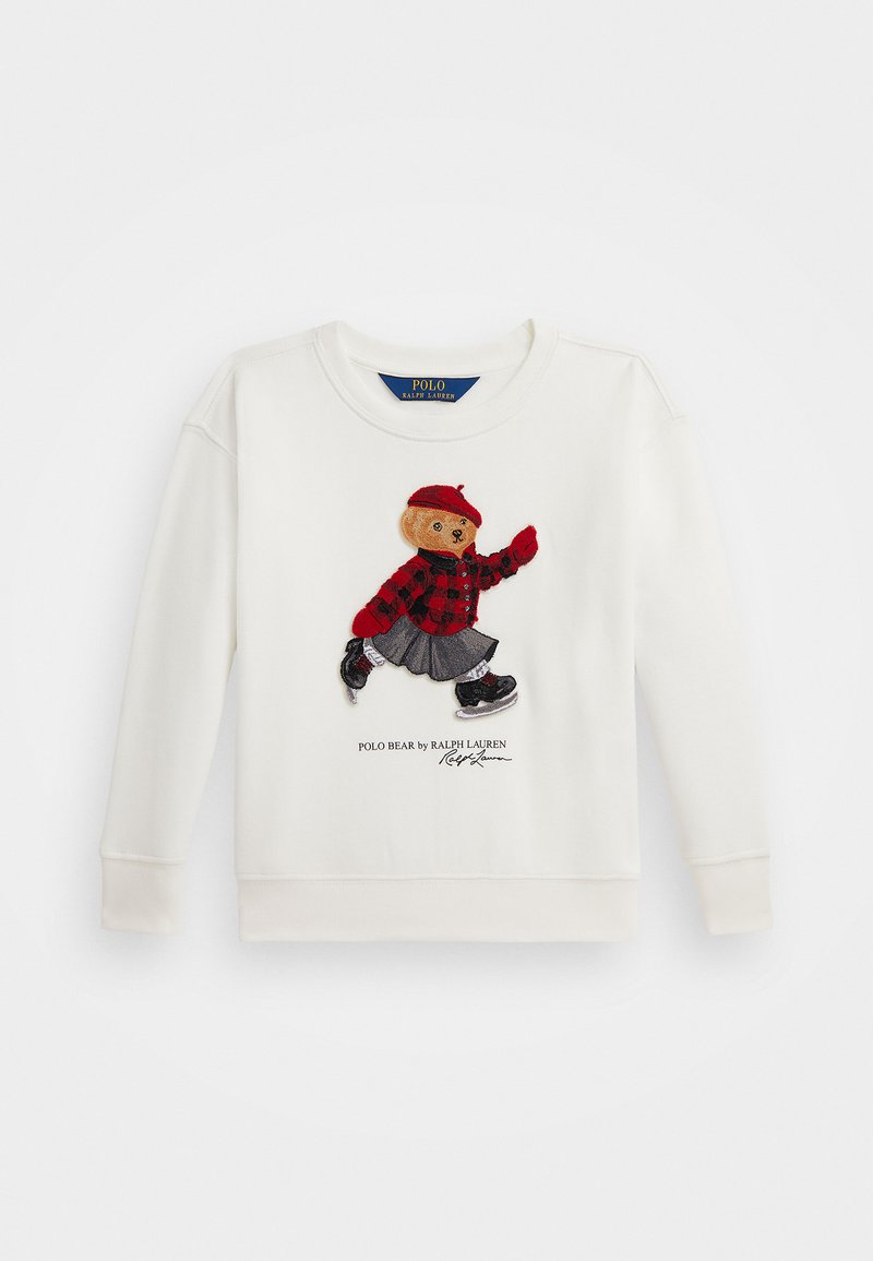 Krémová mikina so zašitou výšivkou medveďa v červenom károvanom tričku, šedom sukni a čiernych teniskách. Obsahuje text "Polo Bear by Ralph Lauren".